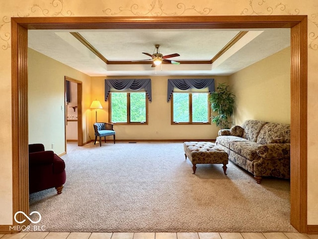 carpeted living area featuring a tray ceiling, a ceiling fan, baseboards, and crown molding
