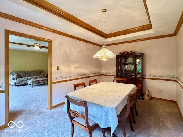 dining area featuring carpet, a tray ceiling, ornamental molding, a chandelier, and ceiling fan