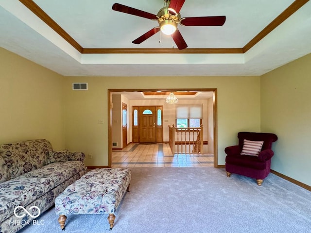 carpeted living room featuring a raised ceiling, ornamental molding, baseboards, and a ceiling fan