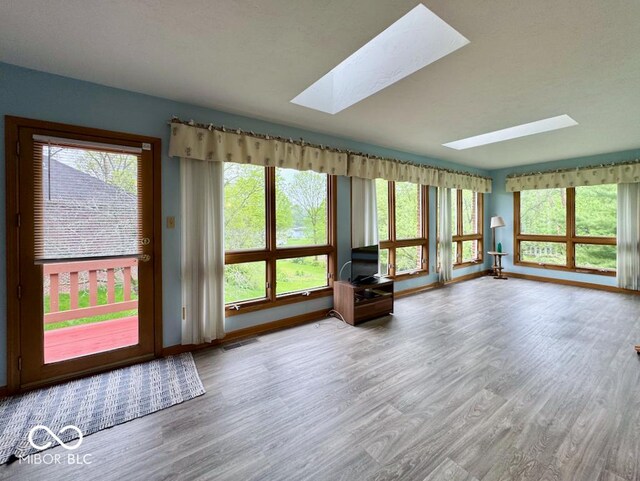 unfurnished living room with a skylight, wood finished floors, baseboards, and plenty of natural light