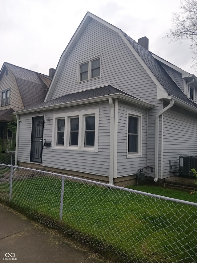 view of property exterior featuring roof with shingles, a gambrel roof, fence private yard, a chimney, and a lawn