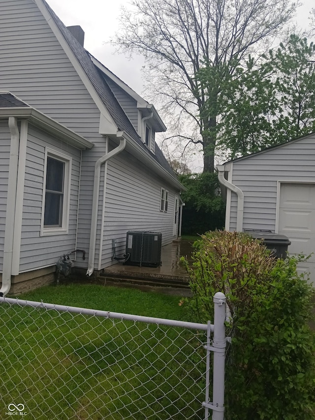 view of side of home featuring central AC unit, roof with shingles, a garage, and fence