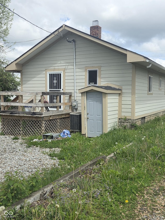 rear view of property featuring a storage unit, cooling unit, a chimney, a deck, and an outbuilding