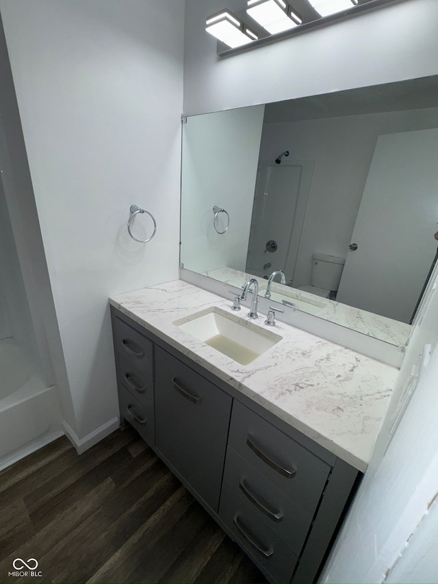 bathroom featuring toilet, wood finished floors, baseboards, vanity, and shower / bathtub combination