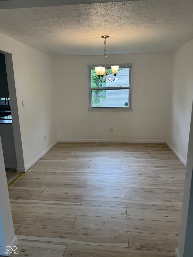 unfurnished dining area with light wood finished floors, a textured ceiling, baseboards, and a notable chandelier