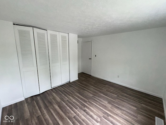 unfurnished bedroom featuring a closet, a textured ceiling, visible vents, baseboards, and dark wood-style floors