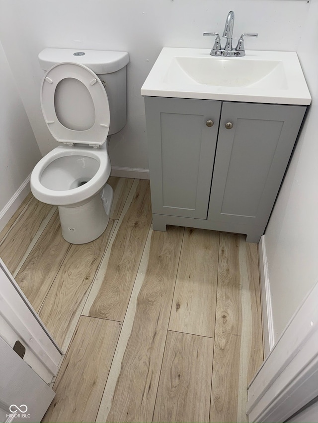 bathroom featuring toilet, baseboards, wood finished floors, and vanity