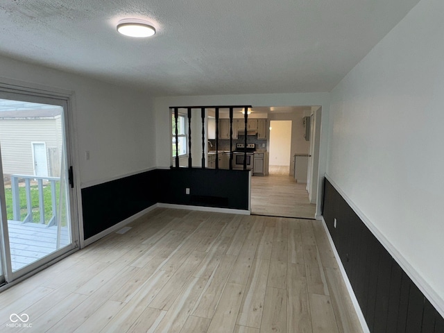spare room with wainscoting, light wood-style flooring, and a textured ceiling