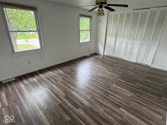 unfurnished bedroom featuring baseboards, dark wood-style flooring, ceiling fan, and visible vents