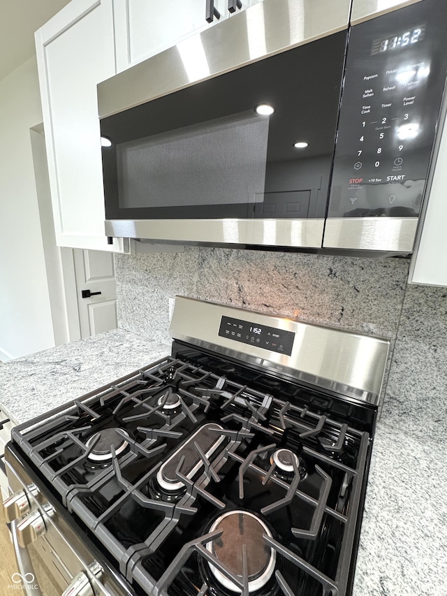 interior details featuring light stone countertops, white cabinetry, decorative backsplash, and appliances with stainless steel finishes