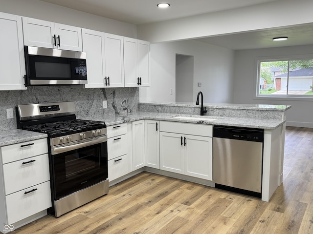 kitchen with white cabinets, appliances with stainless steel finishes, a sink, light wood-style flooring, and a peninsula