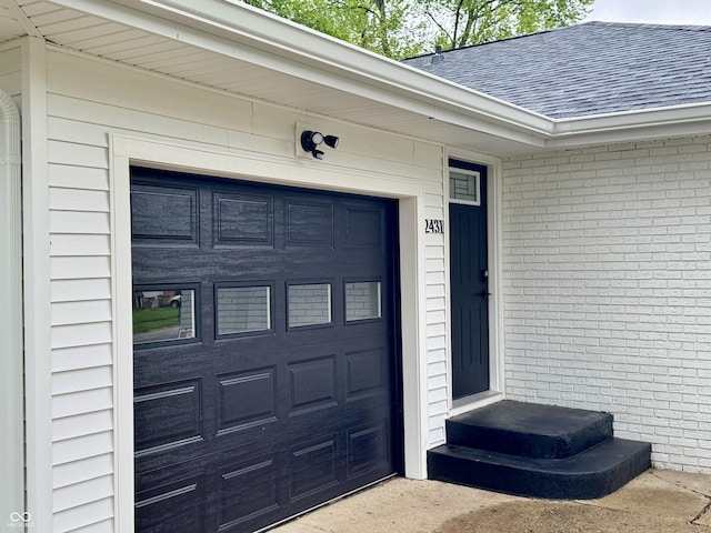 doorway to property featuring brick siding, driveway, roof with shingles, and a garage