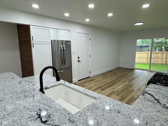 kitchen with wood finished floors, a sink, freestanding refrigerator, light stone counters, and recessed lighting