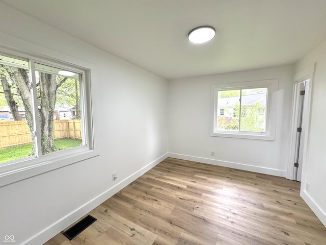 empty room with a wealth of natural light, baseboards, visible vents, and light wood-style floors