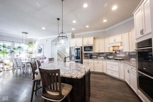 kitchen featuring appliances with stainless steel finishes, ornamental molding, decorative backsplash, a chandelier, and light stone counters