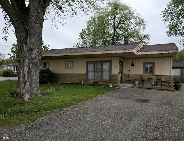 ranch-style house with roof with shingles, a chimney, stone siding, and a front lawn