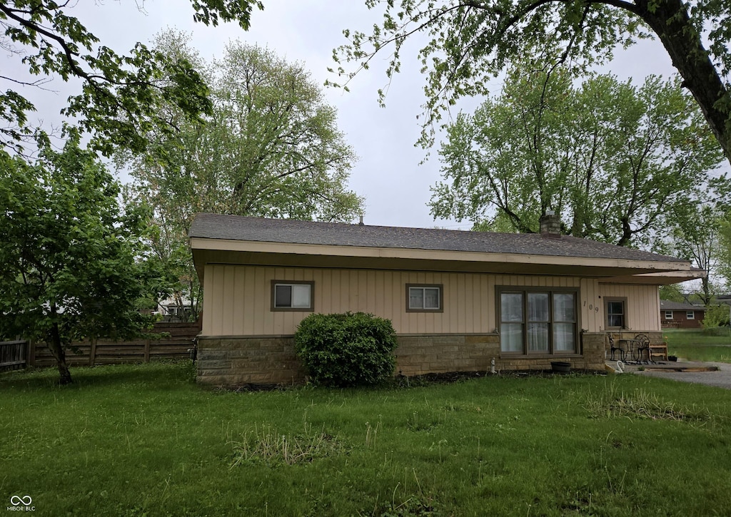 rear view of house with a yard, stone siding, fence, and roof with shingles