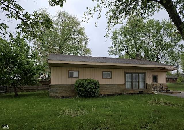 rear view of house with a yard, stone siding, fence, and roof with shingles