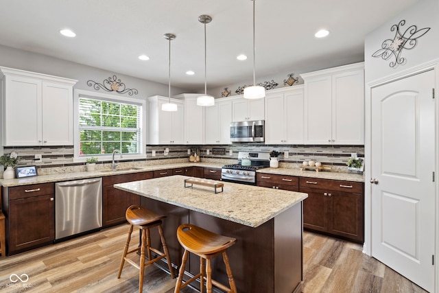 kitchen featuring appliances with stainless steel finishes, tasteful backsplash, a sink, white cabinets, and light wood-style flooring
