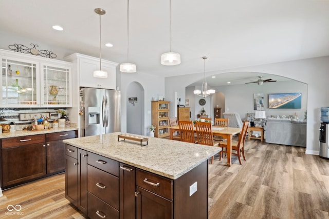 kitchen featuring a ceiling fan, stainless steel refrigerator with ice dispenser, arched walkways, light wood-style floors, and white cabinetry