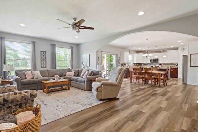 living room with arched walkways, ceiling fan with notable chandelier, recessed lighting, and wood finished floors