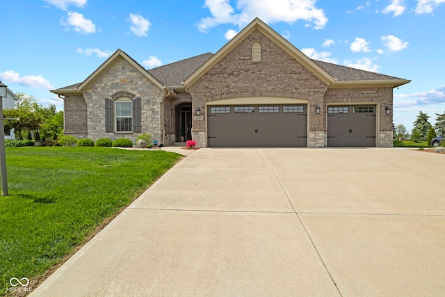 french country inspired facade with a garage, a front lawn, stone siding, brick siding, and driveway