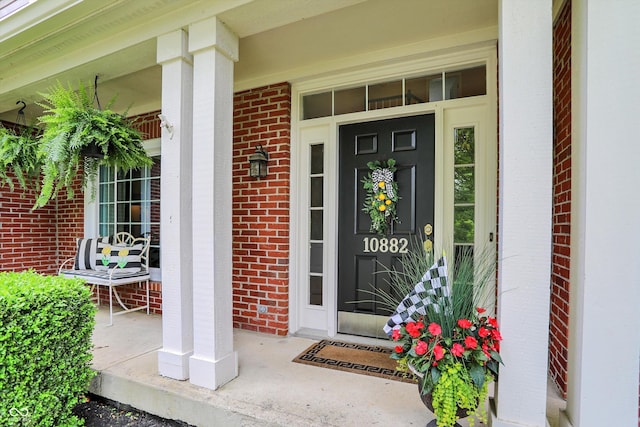 view of exterior entry with a porch and brick siding