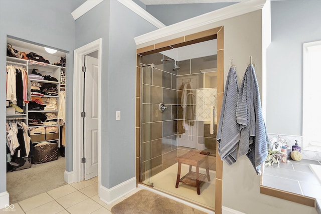 bathroom featuring tile patterned flooring, a stall shower, a walk in closet, crown molding, and baseboards