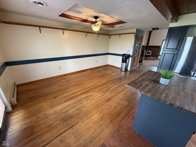 7140 N Michigan Rd, Fairland, IN 46126 - unfurnished living room featuring hardwood / wood-style floors, a wood stove, a ceiling fan, a textured ceiling, and baseboards