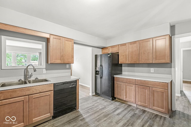 kitchen with a sink, black appliances, light wood finished floors, light countertops, and baseboards