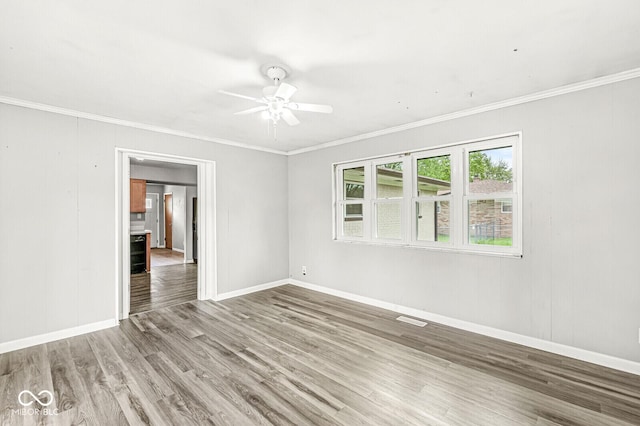empty room featuring wood finished floors, crown molding, visible vents, baseboards, and ceiling fan