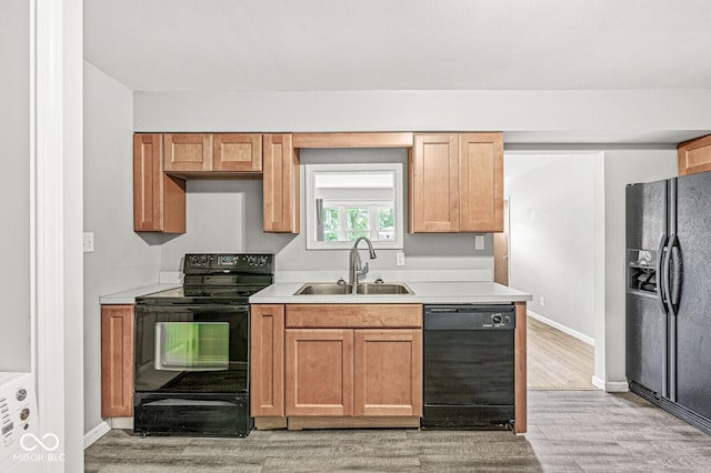 kitchen featuring black appliances, light countertops, light wood-type flooring, and a sink