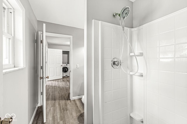 full bath featuring washer / clothes dryer, toilet, wood finished floors, baseboards, and tiled shower