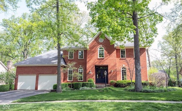 colonial-style house featuring driveway, an attached garage, brick siding, and a front yard