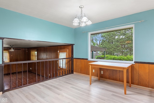 unfurnished dining area featuring wooden walls, a wainscoted wall, wood finished floors, and a notable chandelier