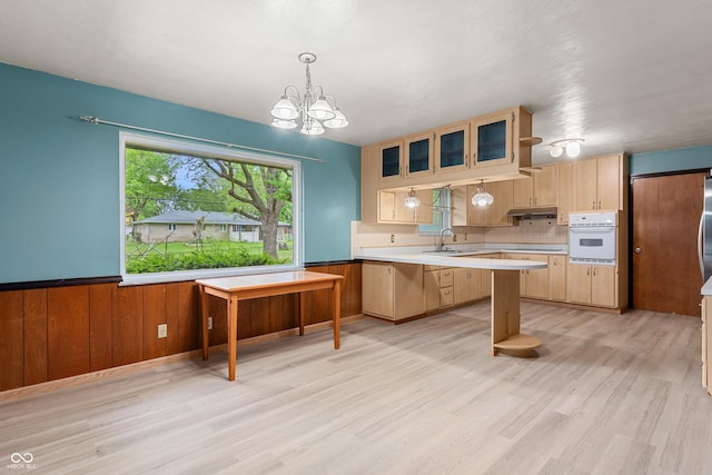 kitchen with light countertops, a wainscoted wall, light wood finished floors, an inviting chandelier, and oven