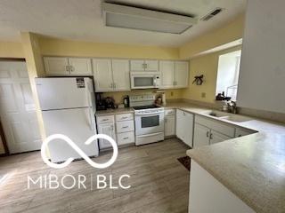 kitchen featuring a sink, white appliances, wood finished floors, visible vents, and light countertops