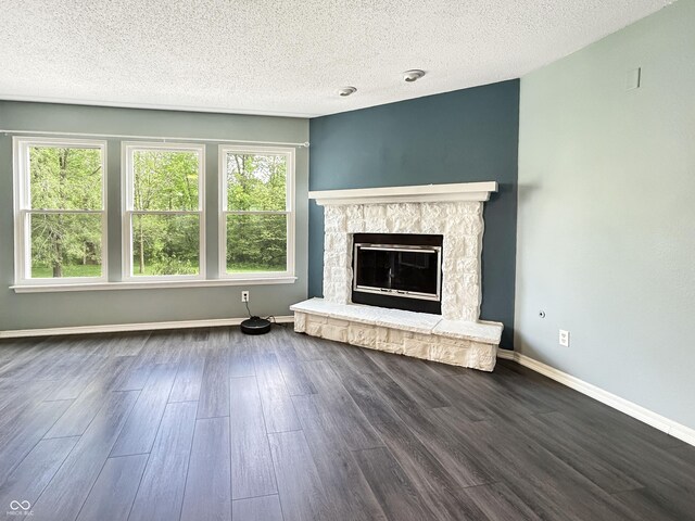 625 Streamside Dr, Greenfield, IN 46140 - unfurnished living room featuring a textured ceiling, plenty of natural light, dark wood finished floors, a stone fireplace, and baseboards
