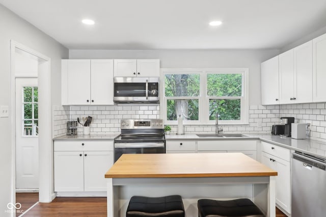 kitchen featuring a breakfast bar area, a sink, wood counters, white cabinetry, and appliances with stainless steel finishes
