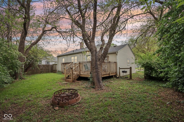 rear view of house featuring an outdoor fire pit, a lawn, fence, and a wooden deck