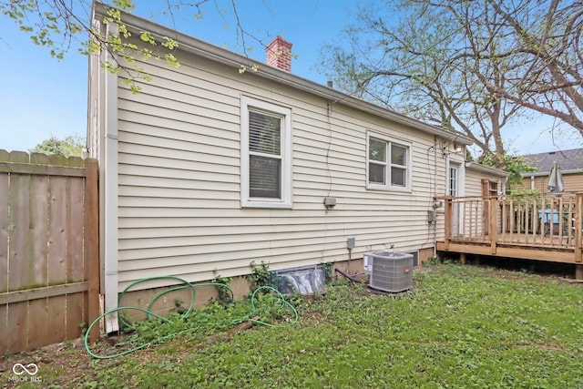 back of house featuring cooling unit, a chimney, a lawn, fence, and a deck