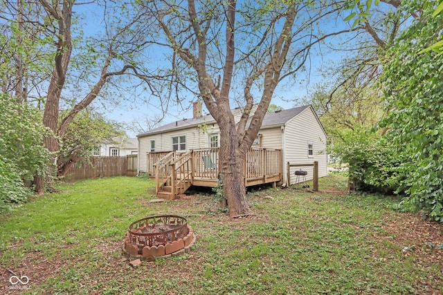 back of property with fence, a deck, a fire pit, a chimney, and a lawn