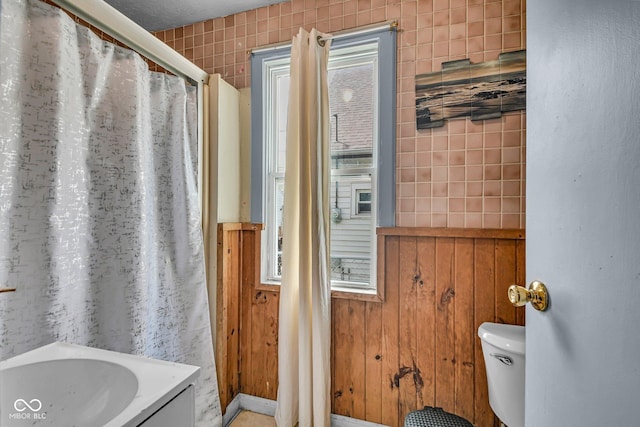 bathroom featuring a shower with curtain, toilet, and wooden walls