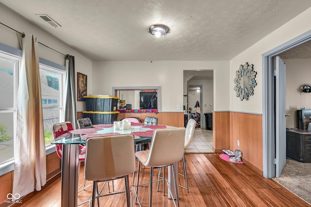 dining space with wainscoting, hardwood / wood-style floors, a textured ceiling, and wooden walls