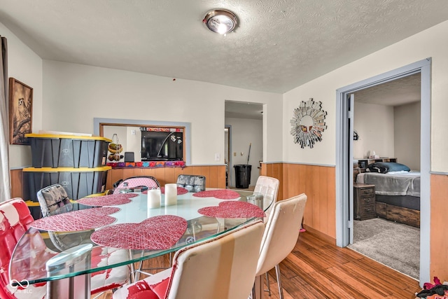 dining room featuring wainscoting, wood finished floors, a textured ceiling, and wood walls
