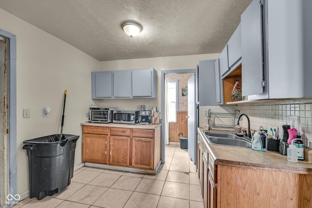 kitchen featuring stainless steel microwave, tasteful backsplash, a sink, a textured ceiling, and light tile patterned floors