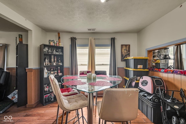 dining area with wood finished floors, a textured ceiling, and a wainscoted wall