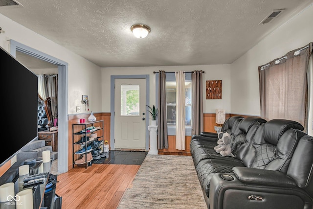 living room featuring wood finished floors, a textured ceiling, and wainscoting