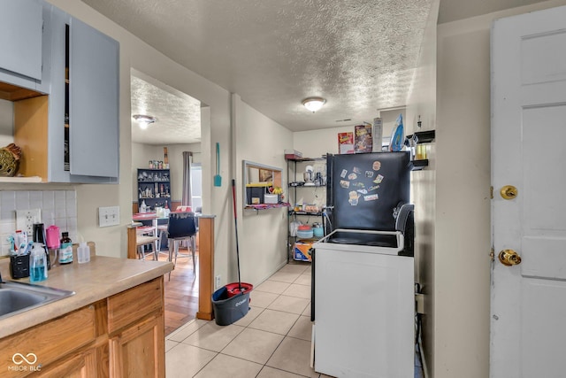 kitchen with freestanding refrigerator, a textured ceiling, light tile patterned flooring, light countertops, and a sink