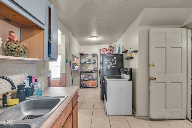 kitchen with a sink, range with electric stovetop, light tile patterned floors, freestanding refrigerator, and brown cabinets